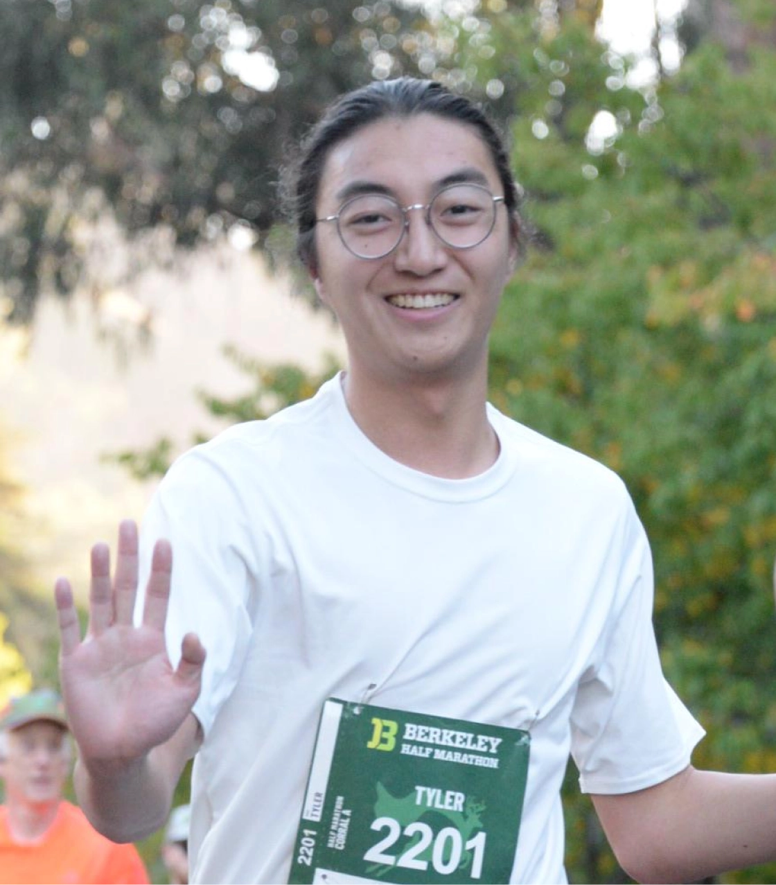 Portrait of the author running and waving at the camera with his right hand. There are trees in the background.